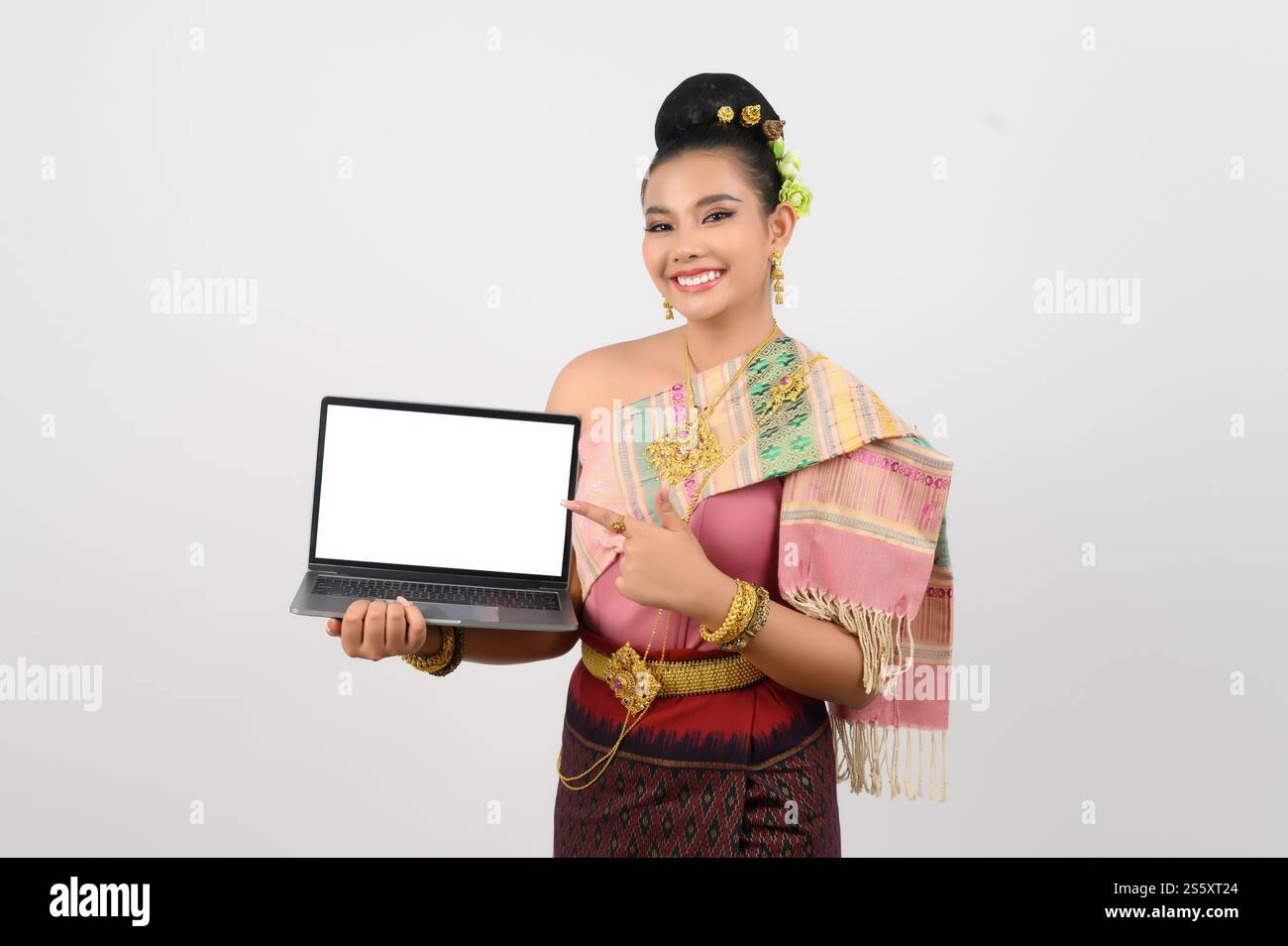 Ritratto di una giovane donna in abbigliamento tradizionale tailandese del nord-est con computer portatile, bella donna asiatica in un bellissimo vestito che regge uno schermo mock-up Foto Stock