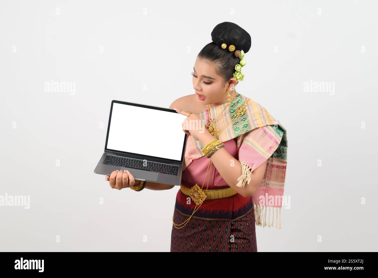 Ritratto di una giovane donna in abbigliamento tradizionale tailandese del nord-est con computer portatile, bella donna asiatica in un bellissimo vestito che regge uno schermo mock-up Foto Stock