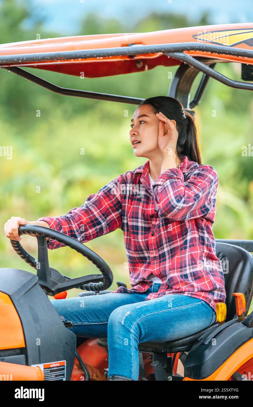Giovane contadina asiatica seduto su una grande macchina trattore in campagna. Tecnologie moderne nella gestione dell'agricoltura e nel concetto di agroalimentare. Foto Stock