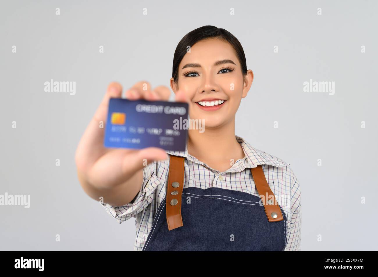 Volto selettivo della giovane donna asiatica in posa uniforme da cameriera con carta di credito in mano, copia spazio per inserire i prodotti per la pubblicità isolata Foto Stock