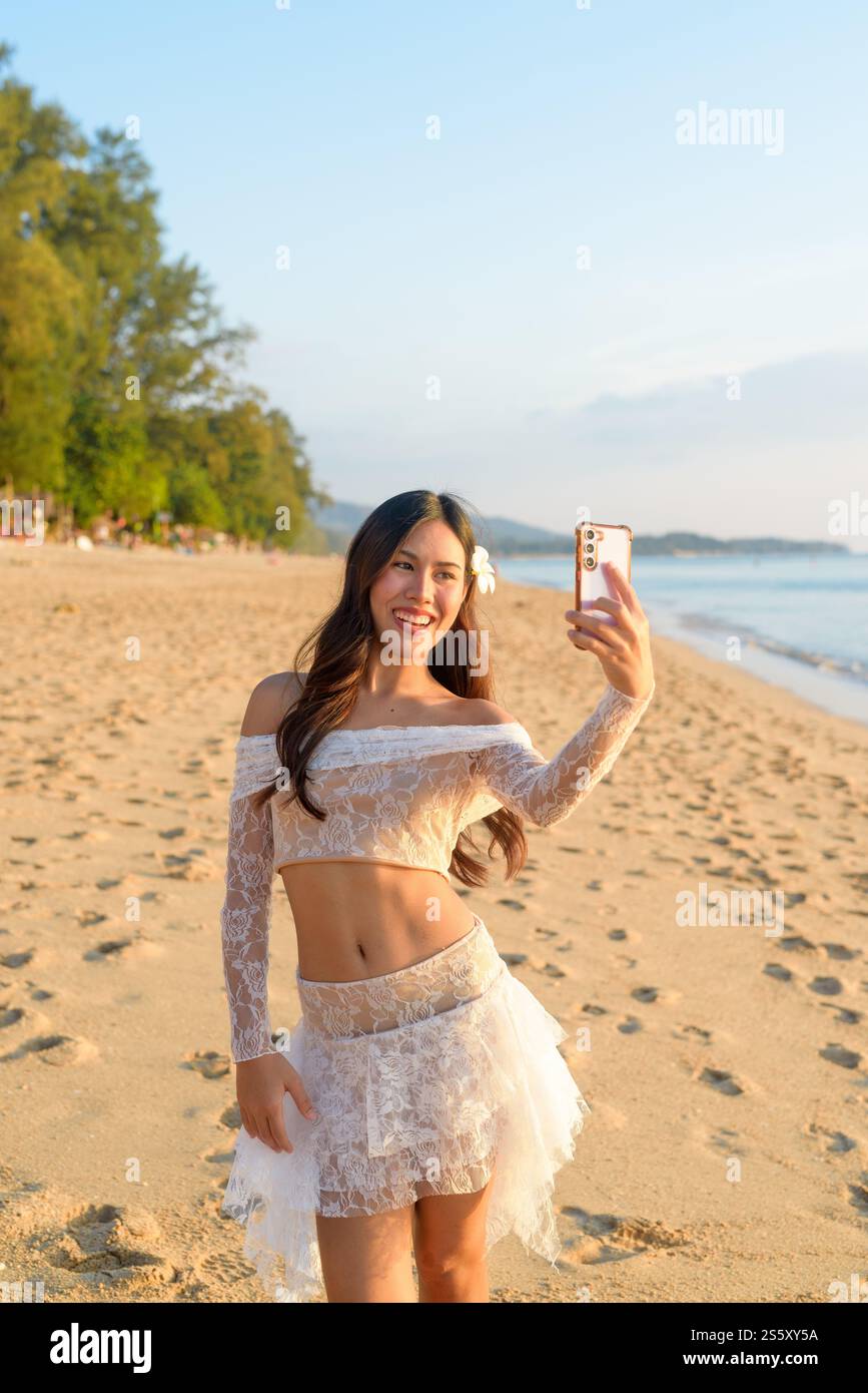 Donna thailandese Vlogging su smartphone in una spiaggia tropicale durante il tramonto Foto Stock
