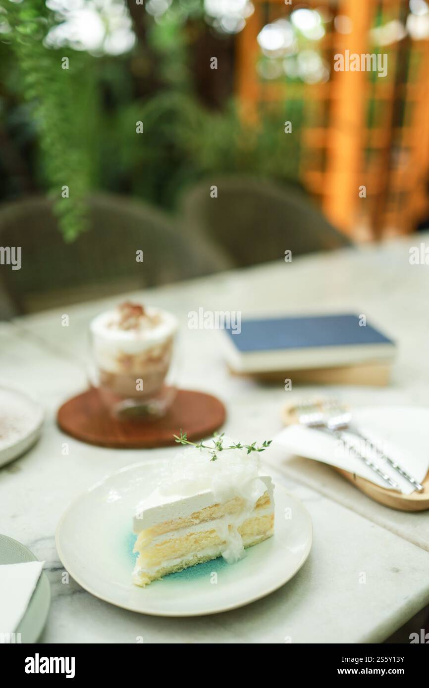 Torta al cocco e caffè in una caffetteria sullo sfondo sfocato. Dessert tradizionale a fette di deliziosa torta a strati di cocco. Foto Stock