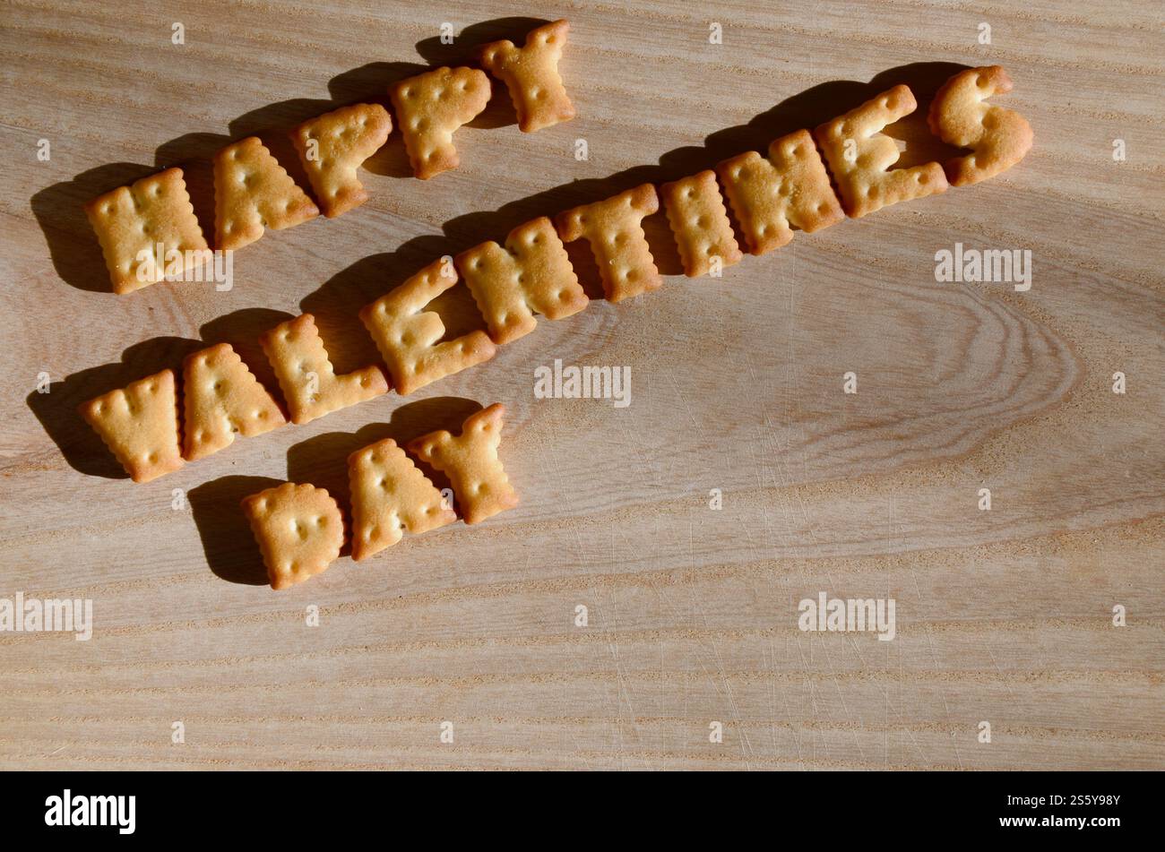 Buon San Valentino. Testo dai cracker salati come lettere inglesi stampate che giacciono su un tagliere di legno. Messaggio, fiancheggiato da lettere commestibili Foto Stock