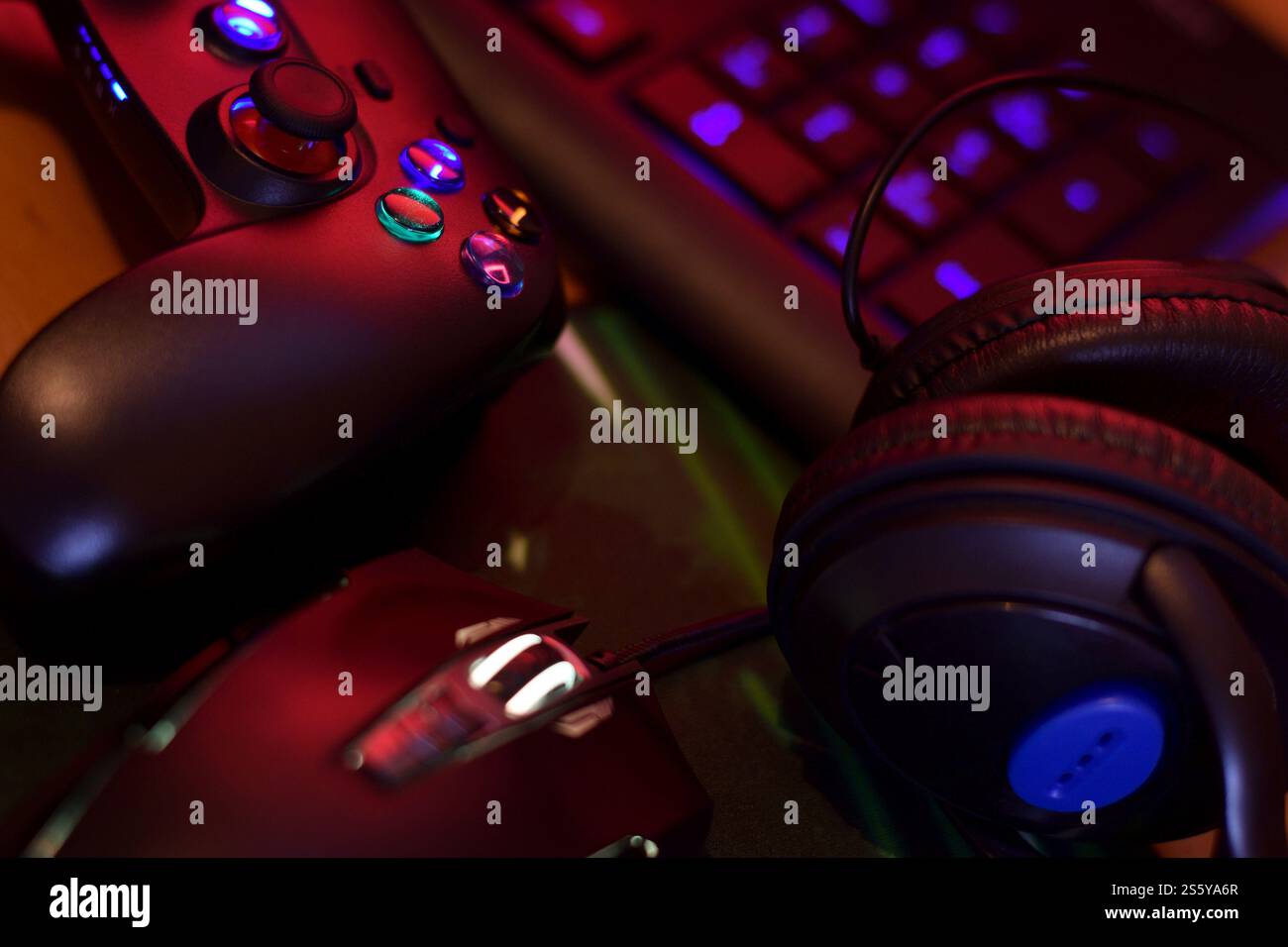 Il moderno gamepad e mouse da gioco è dotato di tastiera e cuffie sul tavolo in primo piano nella scena scura della stanza dei giochi. Composizione dello sfondo per i videogiochi Foto Stock