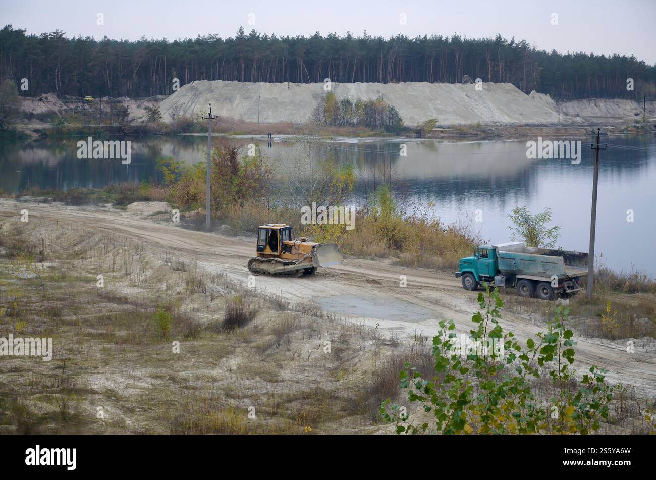 La pala e il dumper Caterpillar lavorano nella cava mineraria a cielo aperto. Macchinari pesanti nella fossa aperta sul fiume. Apripista e dumper su scavo e. Foto Stock