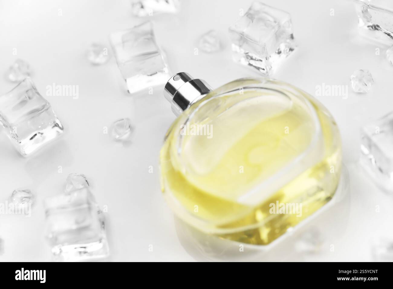 Bottiglia gialla di profumo femminile, fotografia obiettivo della bottiglia di profumo in cubetti di ghiaccio e acqua su un tavolo bianco. Vista dall'alto. Foto del prodotto mockup, Foto Stock