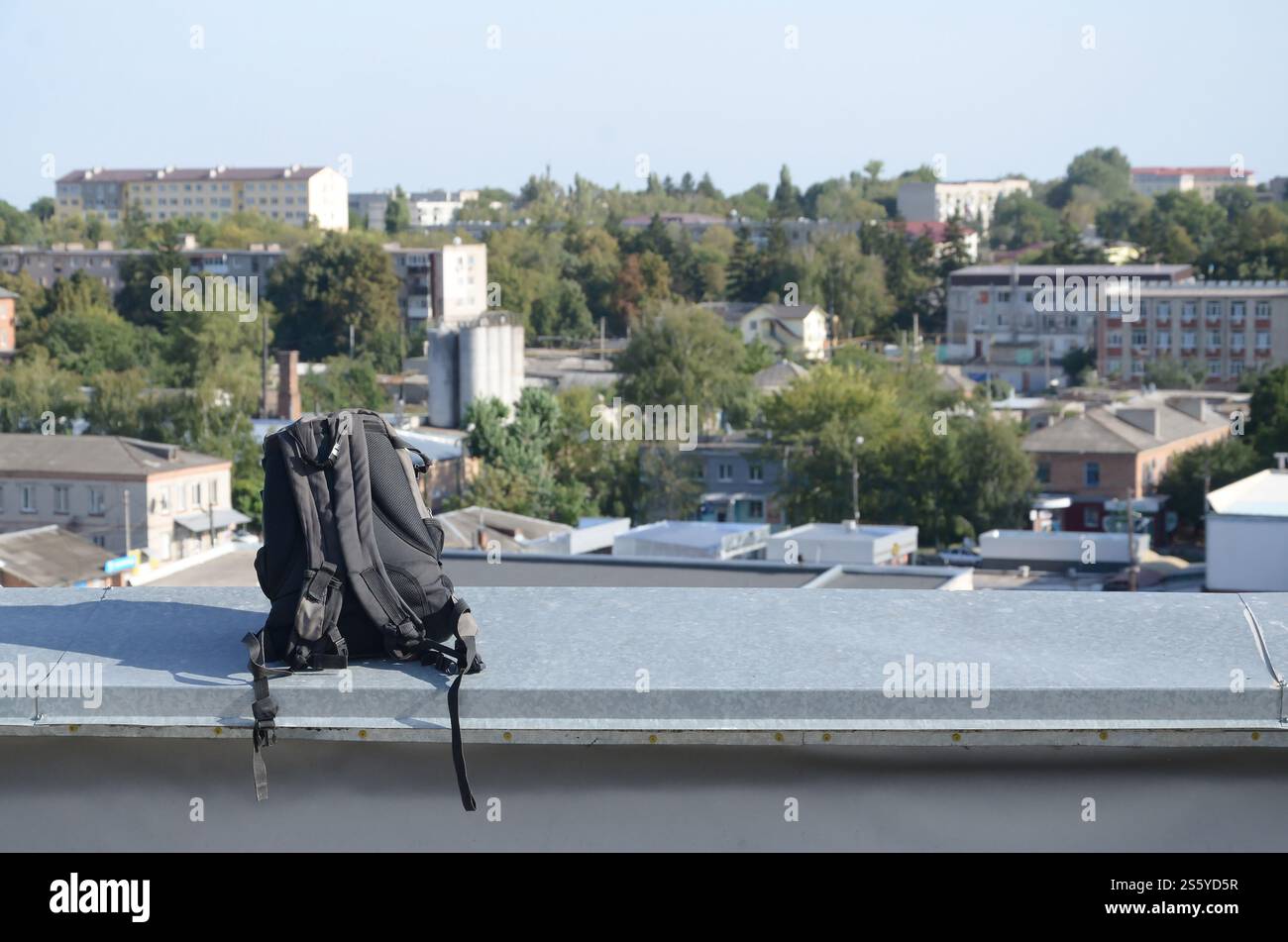Lo zaino nero si trova sul bordo in metallo del tetto di un edificio residenziale a più piani con il sole all'aperto. Lo zaino nero si trova sul bordo metallico di Foto Stock