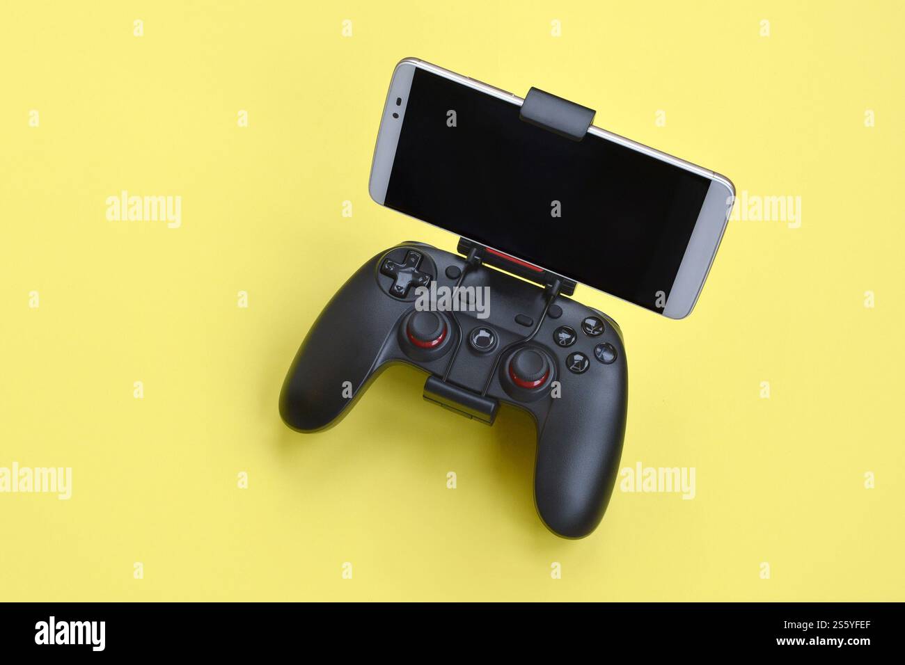 Moderno gamepad nero per smartphone su sfondo giallo primo piano. Dispositivo mobile per videogiochi. Moderno gamepad nero per smartphone su giallo Foto Stock