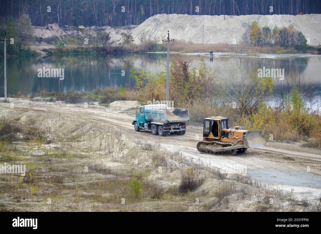 La pala e il dumper Caterpillar lavorano nella cava mineraria a cielo aperto. Macchinari pesanti nella fossa aperta sul fiume. Apripista e dumper su scavo e. Foto Stock