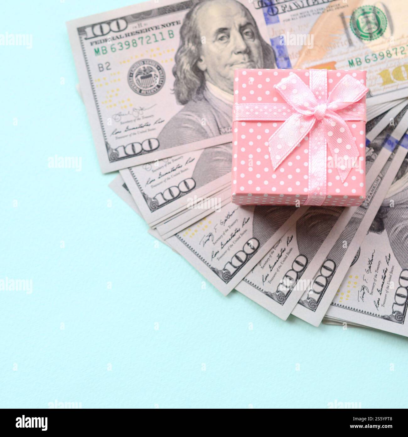 La confezione regalo rosa punteggiata si trova a circa cento banconote da un dollaro su sfondo azzurro. La confezione regalo rosa punteggiata si trova vicino a cento banconote da un dollaro su un blu chiaro Foto Stock