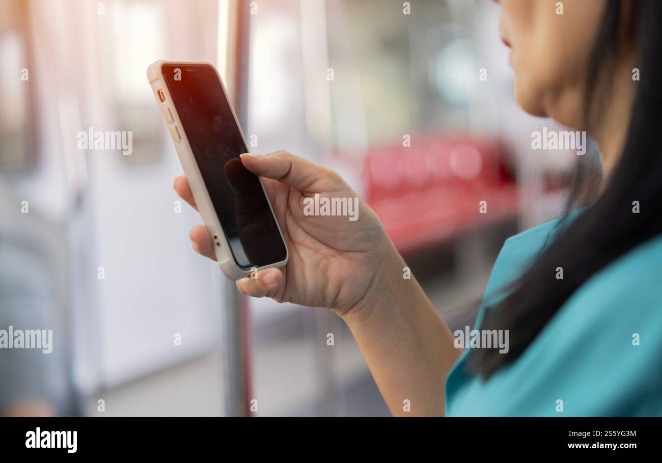 Colpo ritagliato di donna asiatica che usa il cellulare all'interno del compartimento del treno. Messa a fuoco selettiva a portata di mano. Foto Stock