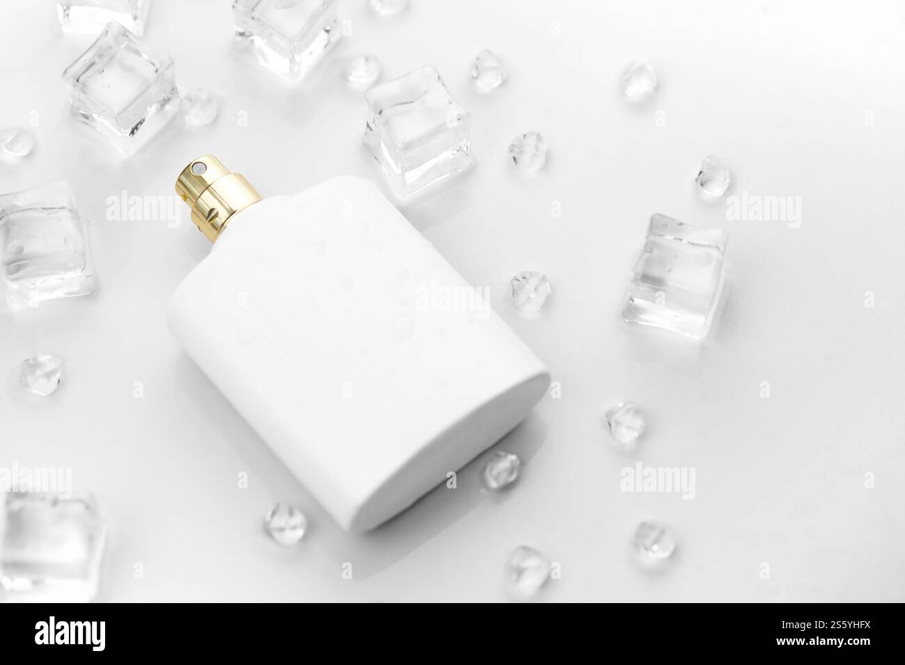 Bottiglia bianca di profumo femminile, fotografia obiettiva di bottiglia di profumo in cubetti di ghiaccio e acqua su tavola bianca. Vista dall'alto. Foto prodotto mockup, Foto Stock