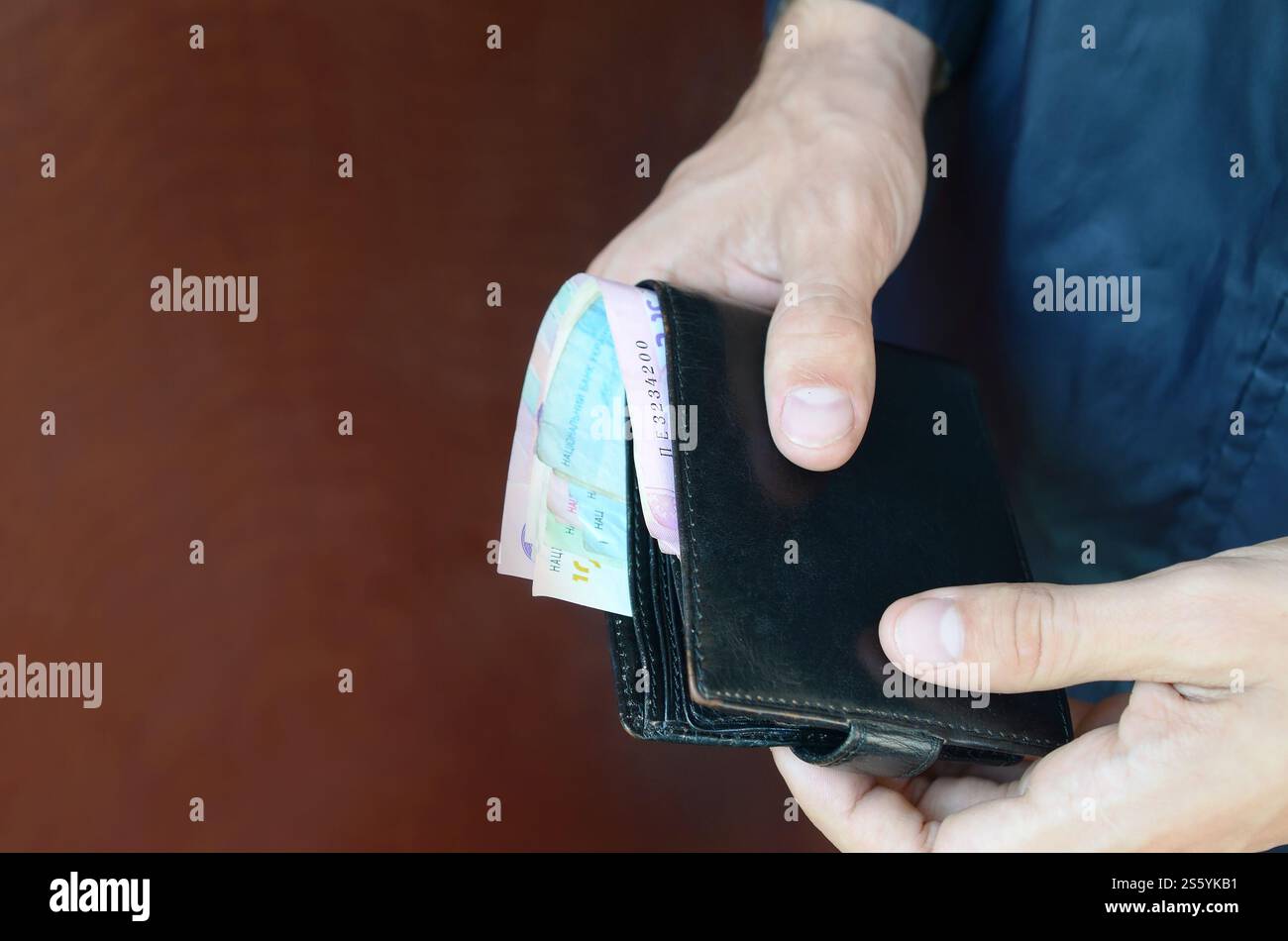 L'uomo tiene in mano un portafoglio in pelle nera con soldi ucraini o un ladro che ha rubato un portafoglio pieno di soldi. Crisi economica Ucraina e concetto di criminalità. Foto Stock