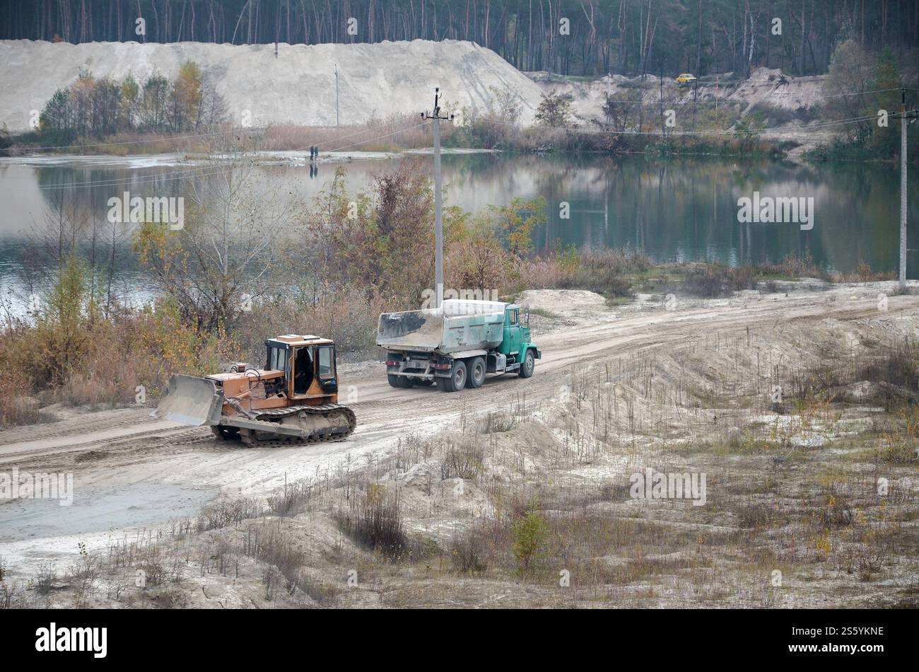 La pala e il dumper Caterpillar lavorano nella cava mineraria a cielo aperto. Macchinari pesanti nella fossa aperta sul fiume. Apripista e dumper su scavo e. Foto Stock
