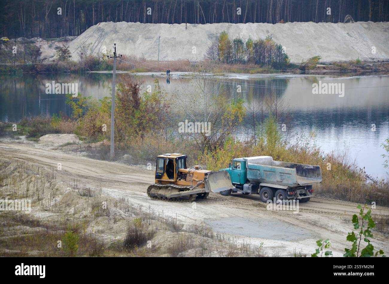 La pala e il dumper Caterpillar lavorano nella cava mineraria a cielo aperto. Macchinari pesanti nella fossa aperta sul fiume. Apripista e dumper su scavo e. Foto Stock