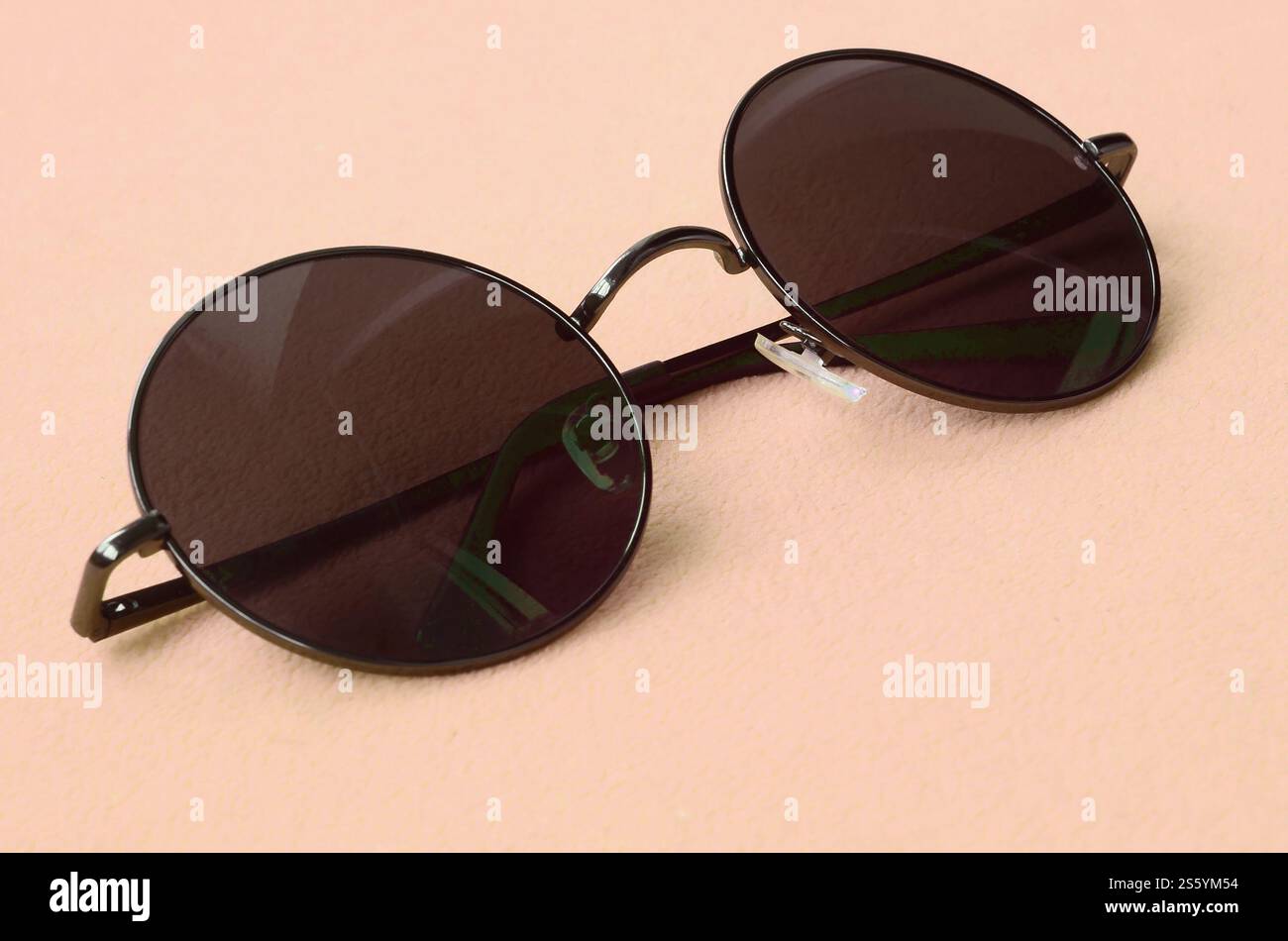 Gli eleganti occhiali da sole neri con occhiali rotondi si appoggiano su una coperta realizzata in morbido e soffice tessuto in pile arancione chiaro. Elegante immagine di sfondo in Foto Stock