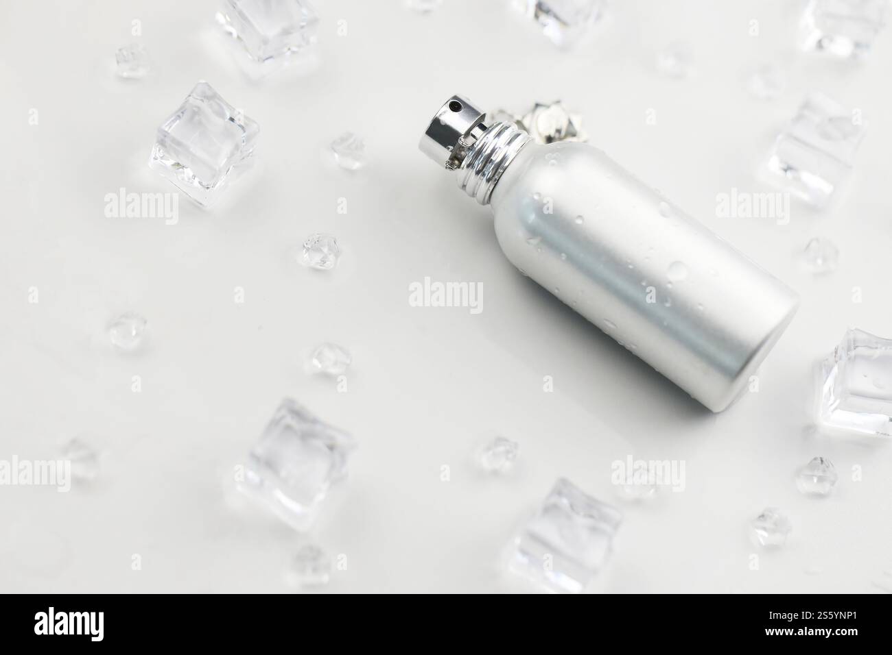 Bottiglia argentata di profumo femminile, Fotografia obiettivo di bottiglia di profumo metallico in cubetti di ghiaccio e acqua su tavola bianca. Vista dall'alto. Prodotto mockup Foto Stock