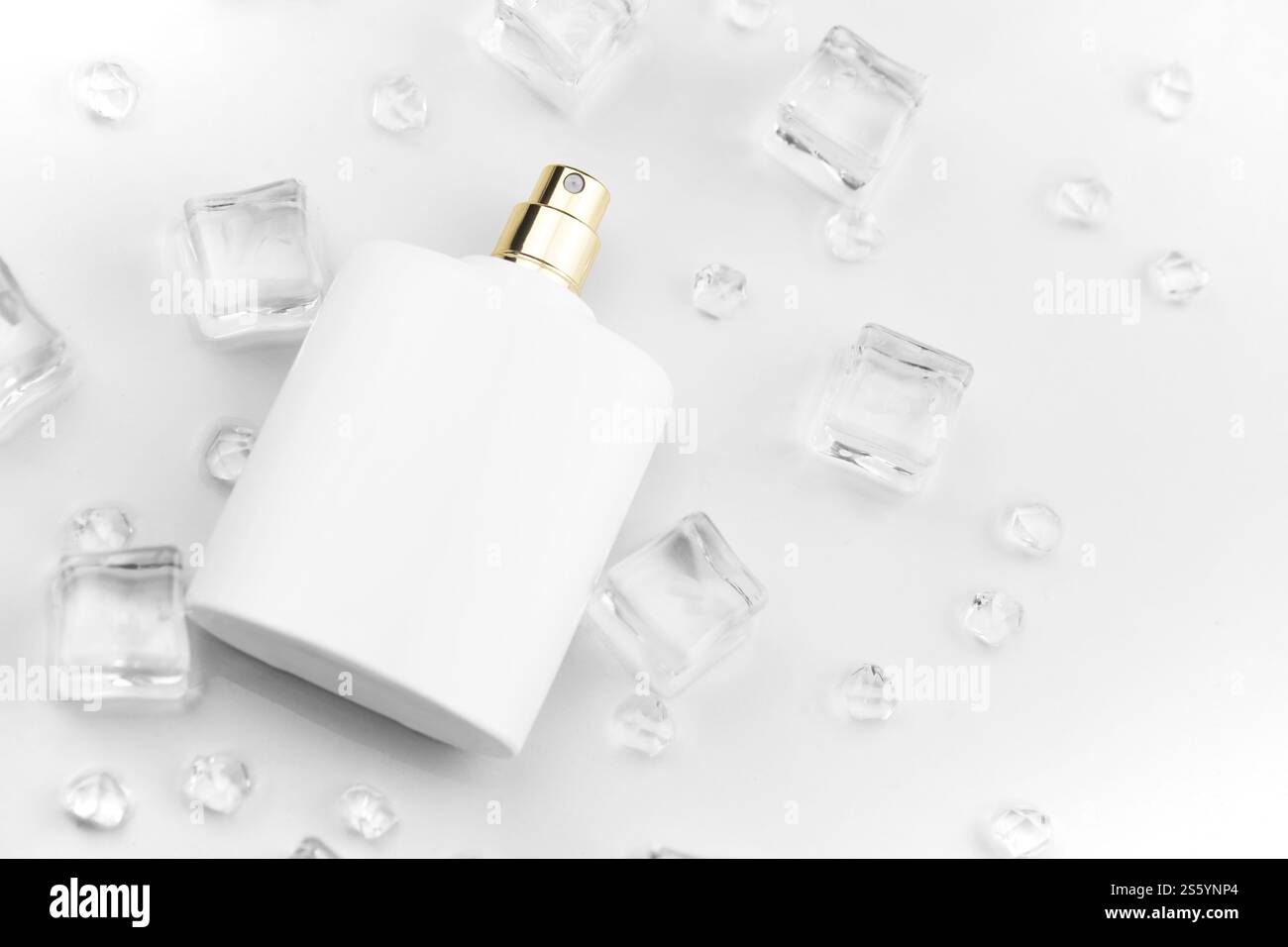 Bottiglia bianca di profumo femminile, fotografia obiettiva di bottiglia di profumo in cubetti di ghiaccio e acqua su tavola bianca. Vista dall'alto. Foto prodotto mockup, Foto Stock