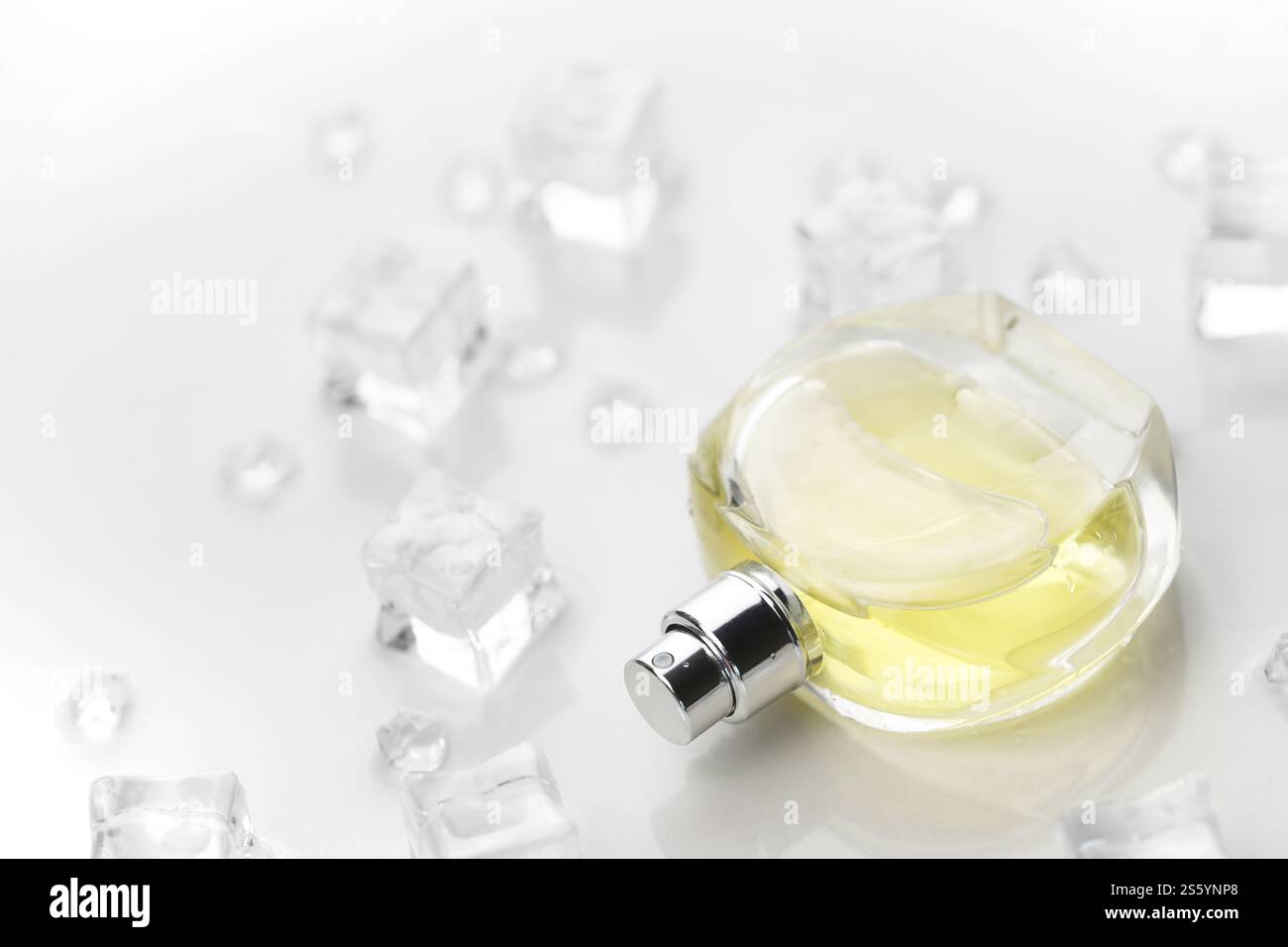 Bottiglia gialla di profumo femminile, fotografia obiettivo della bottiglia di profumo in cubetti di ghiaccio e acqua su un tavolo bianco. Vista dall'alto. Foto del prodotto mockup, Foto Stock