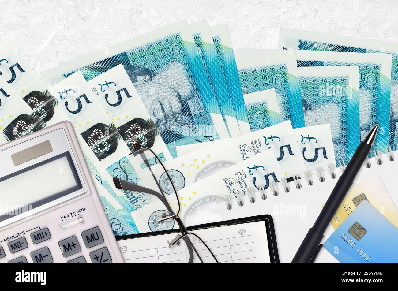 Banconote da 5 sterline inglesi e calcolatrice con occhiali e penna. Concetto di stagione del pagamento delle imposte o soluzioni di investimento. Pianificazione finanziaria o contabile Foto Stock