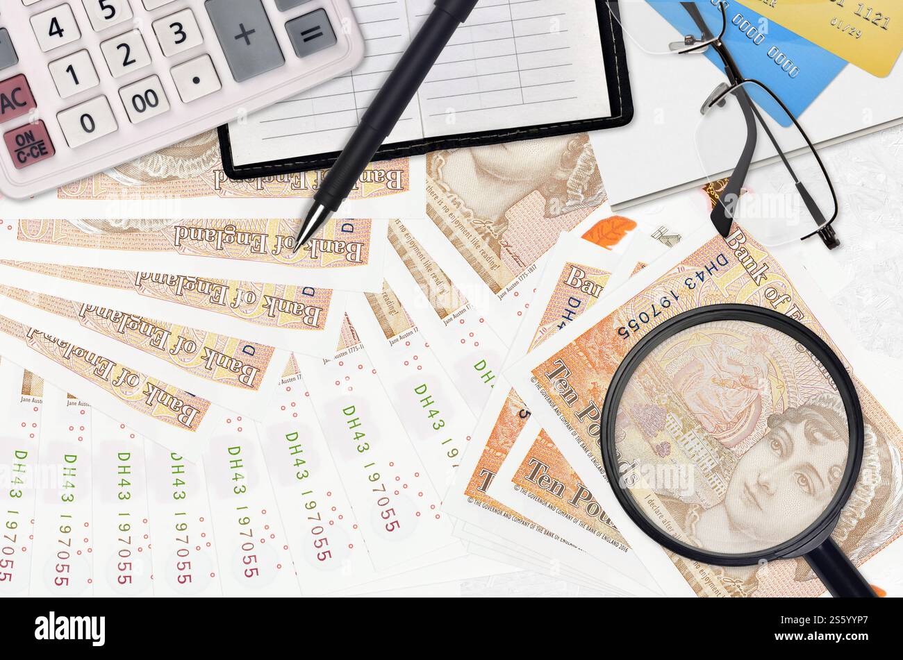 Banconote da 10 sterline inglesi e calcolatrice con occhiali e penna. Concetto di stagione del pagamento delle imposte o soluzioni di investimento. Alla ricerca di un lavoro con stipendio elevato Foto Stock