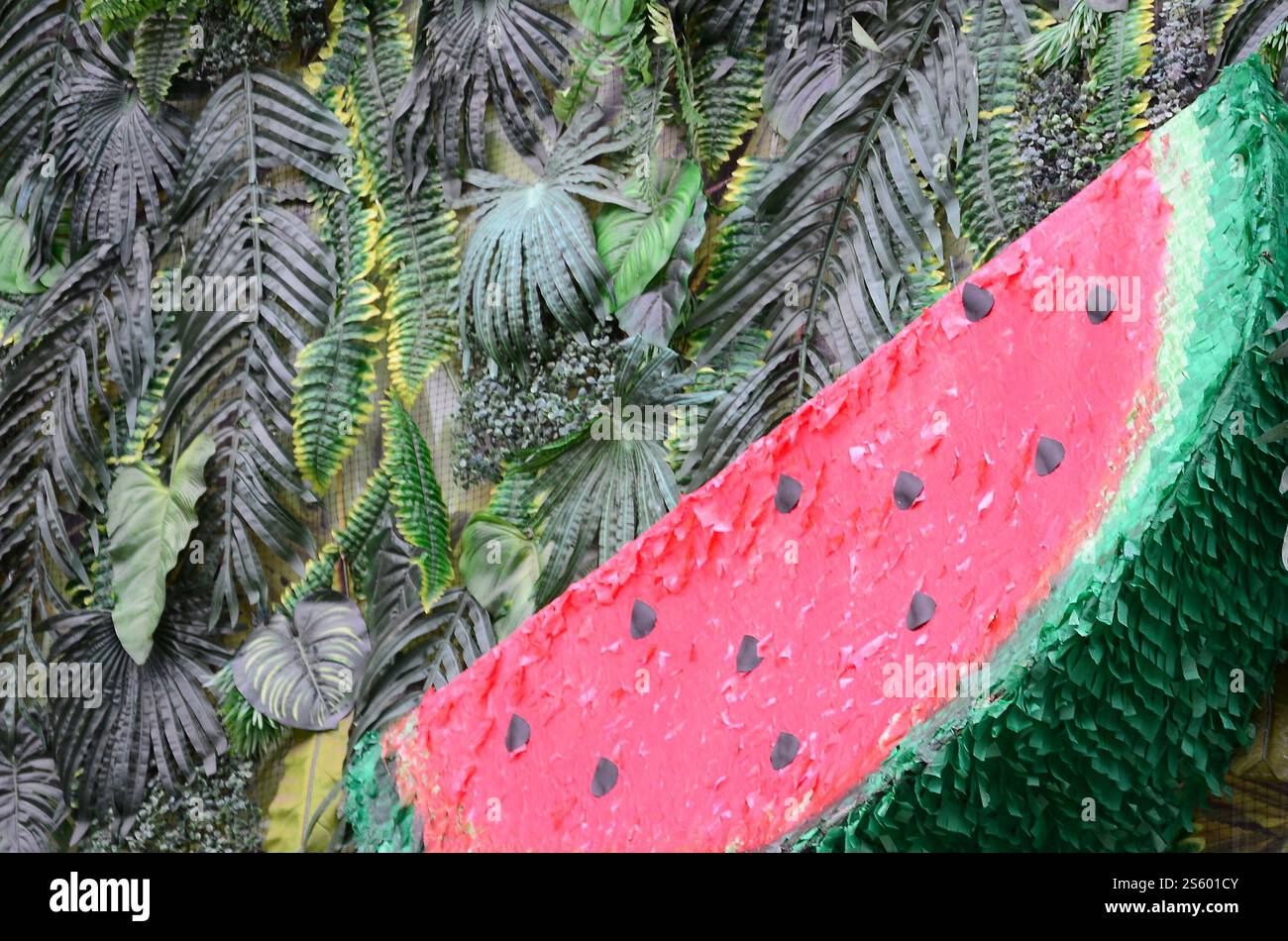 Motivo tropicale con foglie di giungla e fondo floreale di frutta anguria. Fetta di anguria di plastica con foglia di palma. Motivo tropicale con giungla Foto Stock
