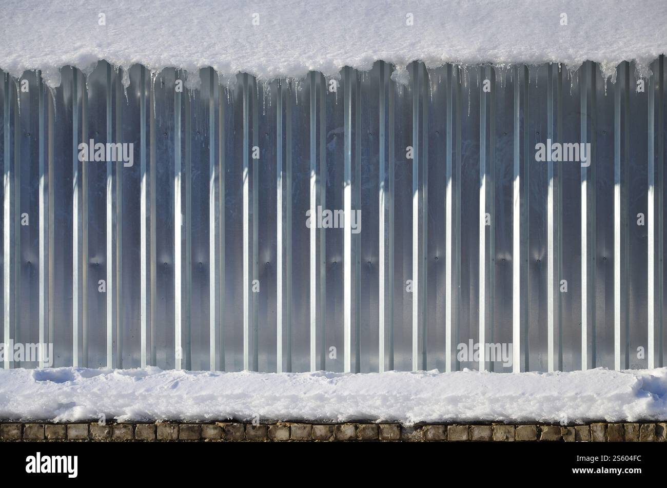 La texture di metallo lucido e goffrato parete nella luce del sole in inverno con uno spesso strato di neve sulla sommità di esso. Foto Stock