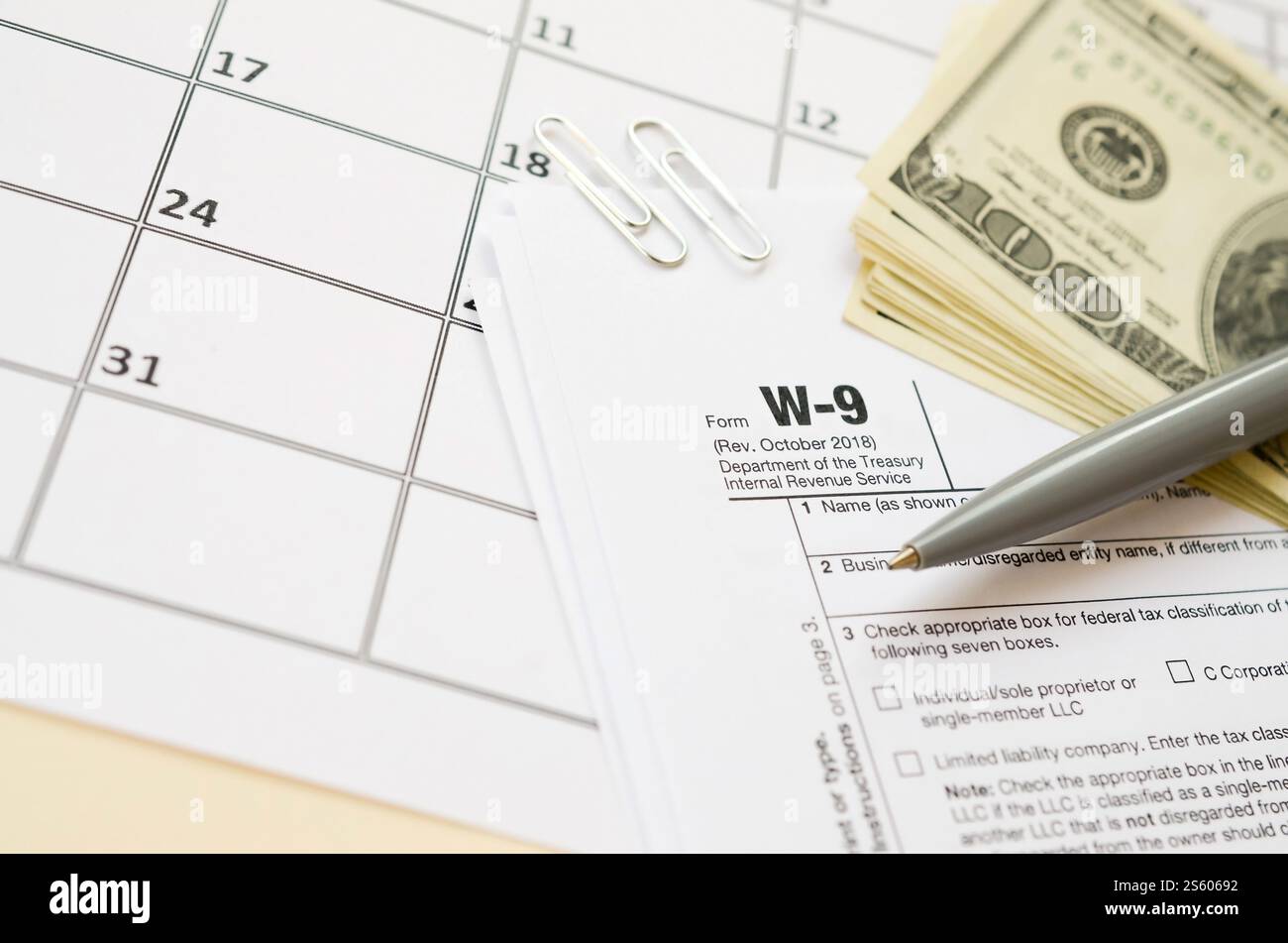 Modulo IRS W-9 richiesta di numero di identificazione contribuente e certificato vuoto si trova con la penna e molte banconote da cento dollari sulla pagina del calendario. Tassa Foto Stock