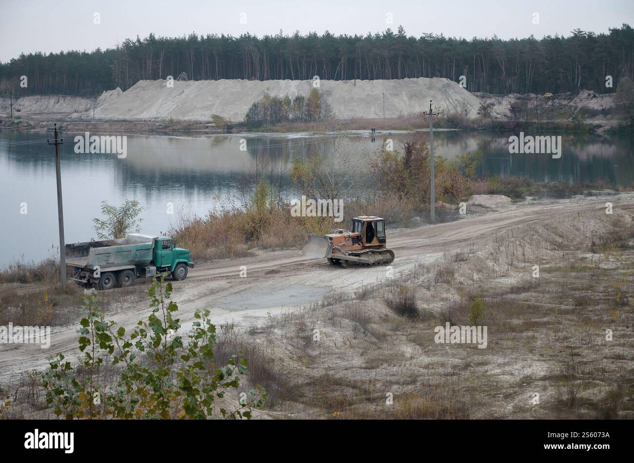 La pala e il dumper Caterpillar lavorano nella cava mineraria a cielo aperto. Macchinari pesanti nella fossa aperta sul fiume. Apripista e dumper su scavo e. Foto Stock