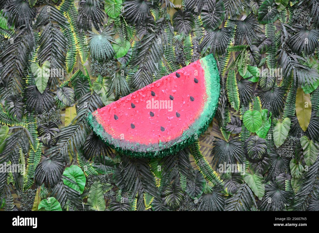 Motivo tropicale con foglie di giungla e fondo floreale di frutta anguria. Fetta di anguria di plastica con foglia di palma. Motivo tropicale con giungla Foto Stock