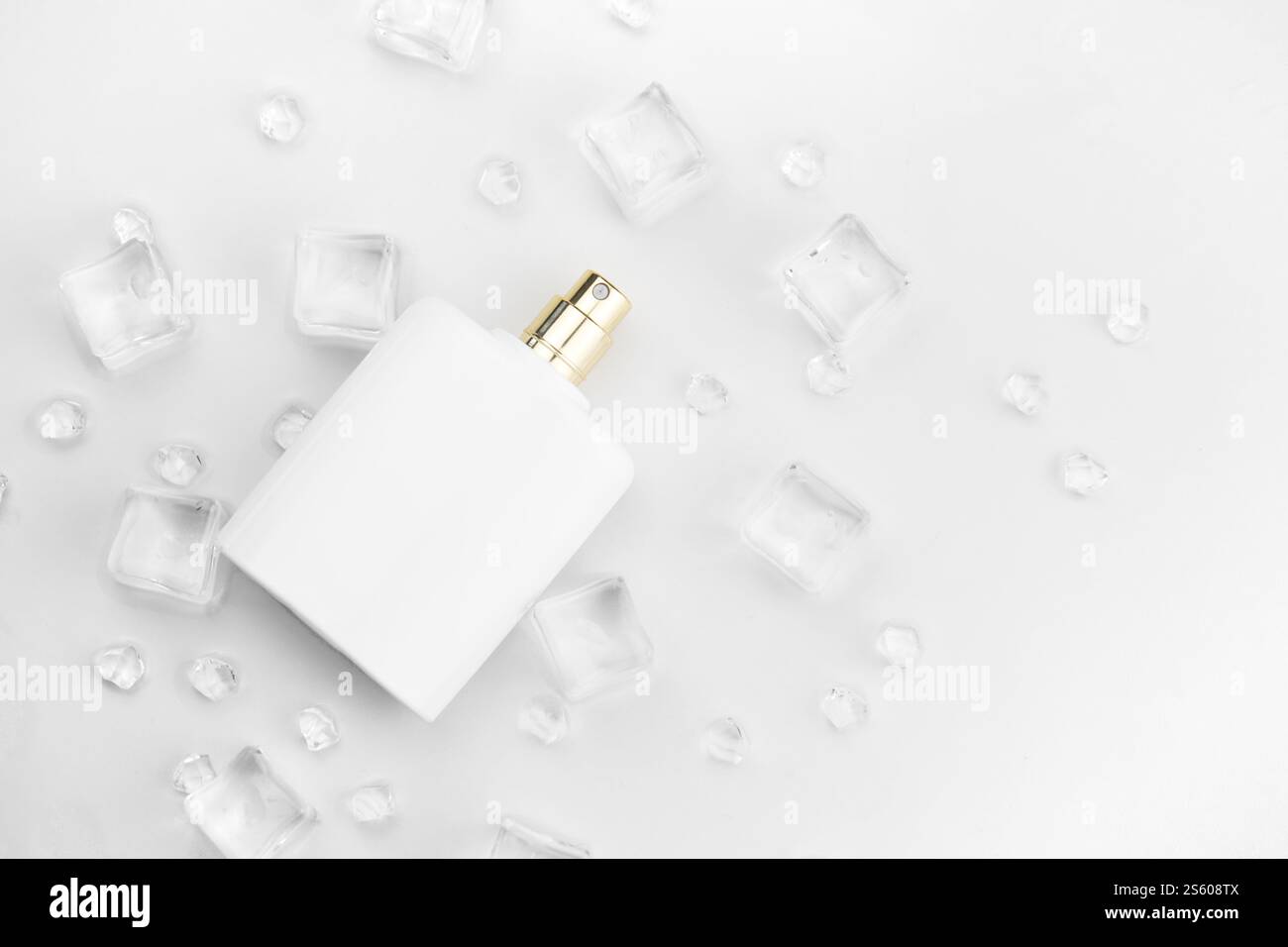 Bottiglia bianca di profumo femminile, fotografia obiettiva di bottiglia di profumo in cubetti di ghiaccio e acqua su tavola bianca. Vista dall'alto. Foto prodotto mockup, Foto Stock