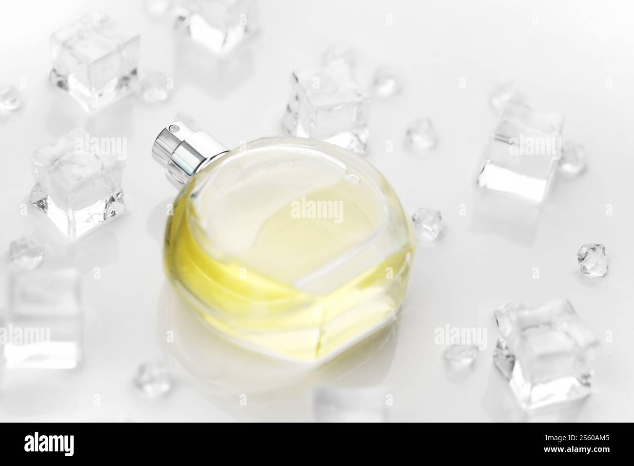 Bottiglia gialla di profumo femminile, fotografia obiettivo della bottiglia di profumo in cubetti di ghiaccio e acqua su un tavolo bianco. Vista dall'alto. Foto del prodotto mockup, Foto Stock