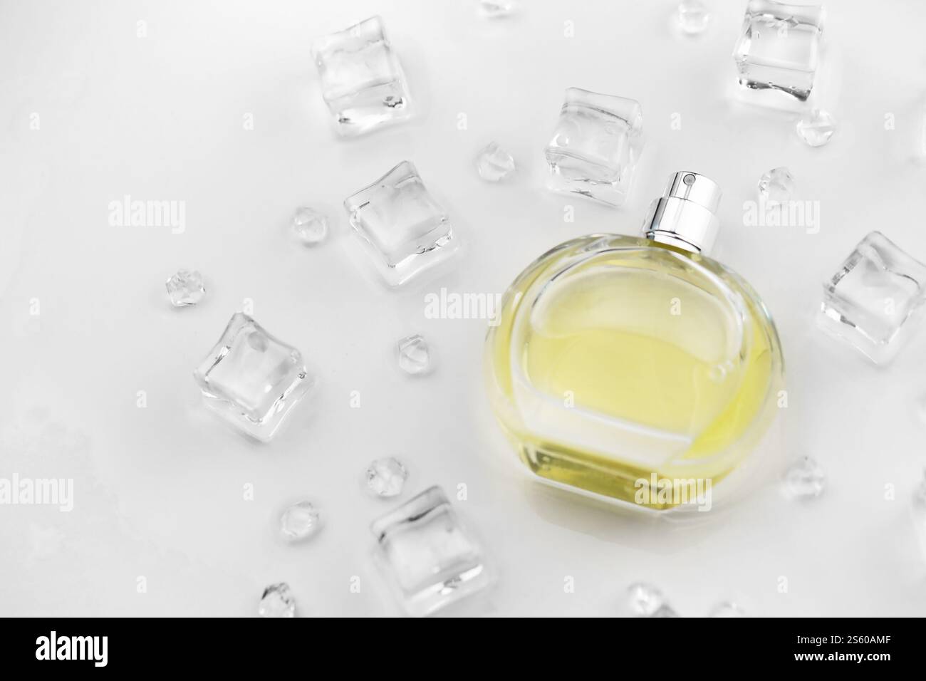 Bottiglia gialla di profumo femminile, fotografia obiettivo della bottiglia di profumo in cubetti di ghiaccio e acqua su un tavolo bianco. Vista dall'alto. Foto del prodotto mockup, Foto Stock