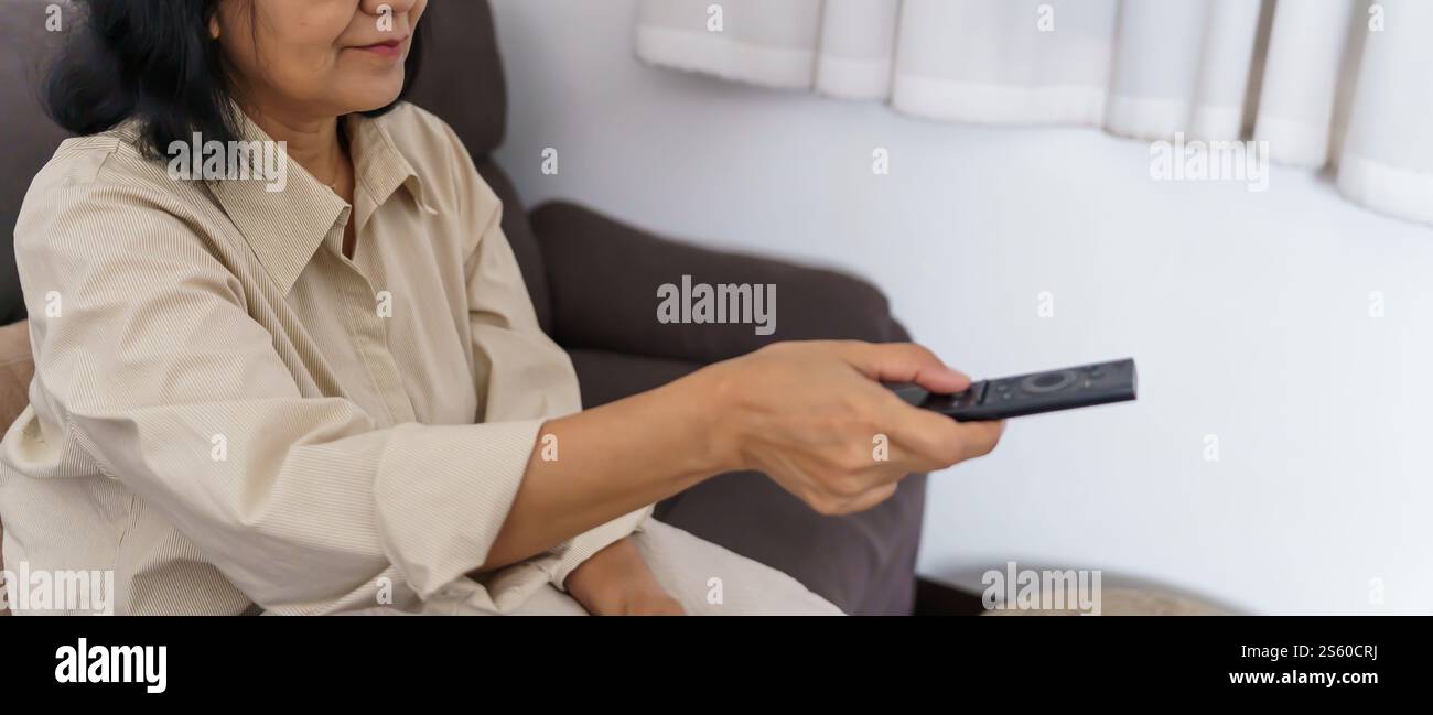 Donna anziana che guarda la smart TV e usa il telecomando che tiene la mano la televisione telecomando audio la donna asiatica di mezza età la televisione di film Foto Stock