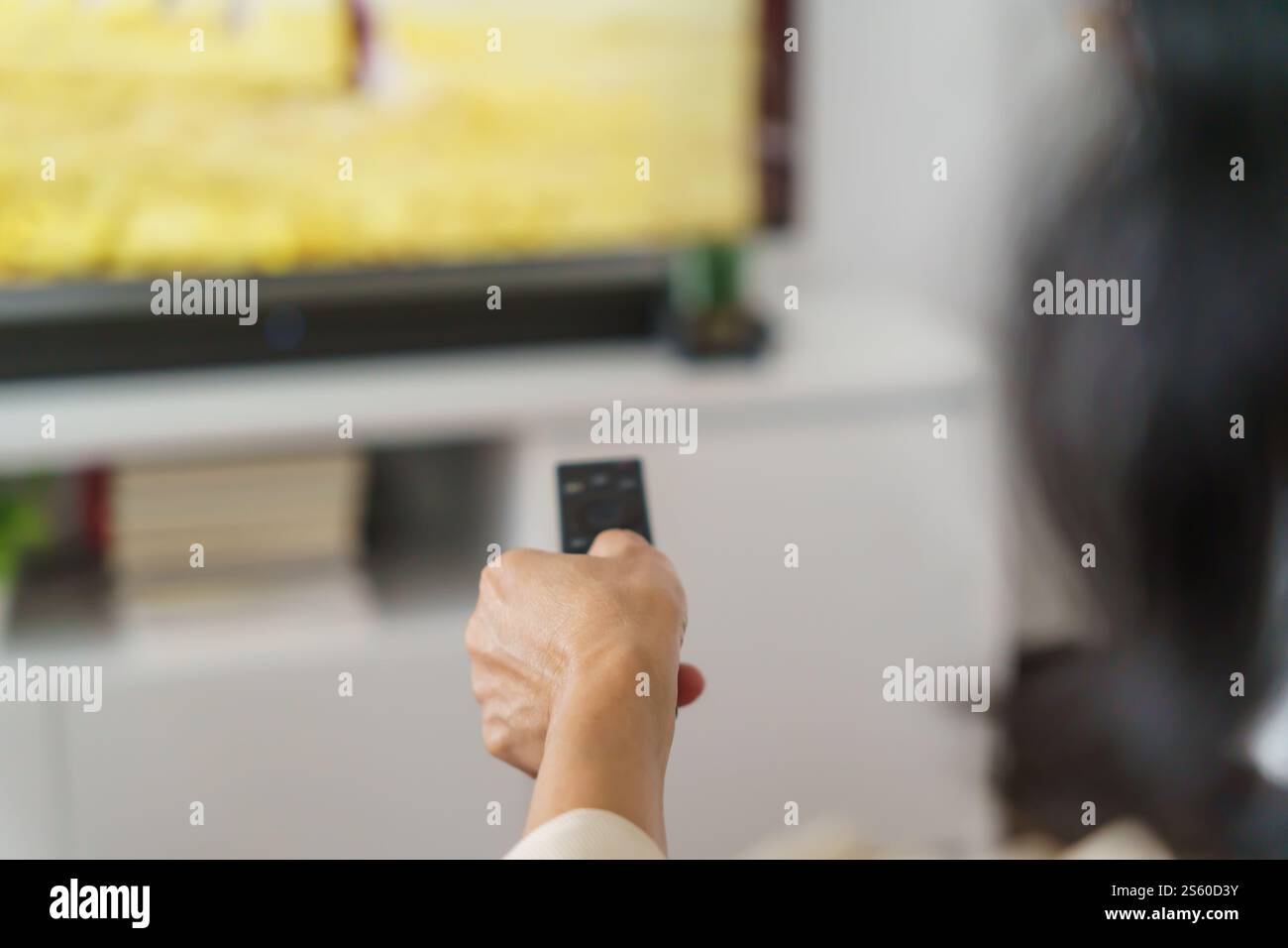 Donna anziana che guarda la smart TV e usa il telecomando che tiene la mano la televisione telecomando audio la donna asiatica di mezza età la televisione di film Foto Stock