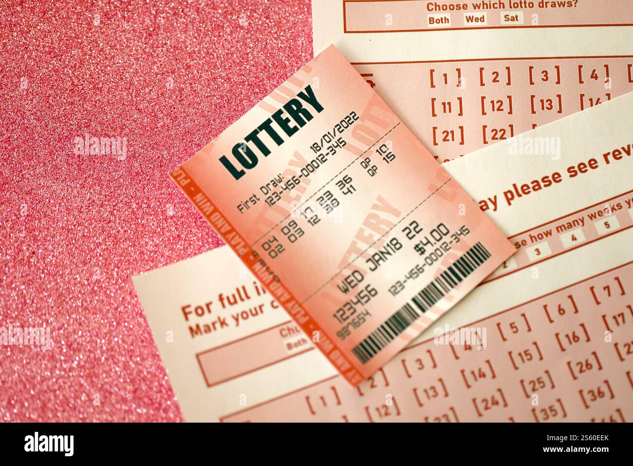 Il biglietto della lotteria rossa si trova su fogli da gioco rosa con i numeri da contrassegnare per giocare alla lotteria. Concetto di gioco alla lotteria o dipendenza dal gioco d'azzardo. Primo piano Foto Stock