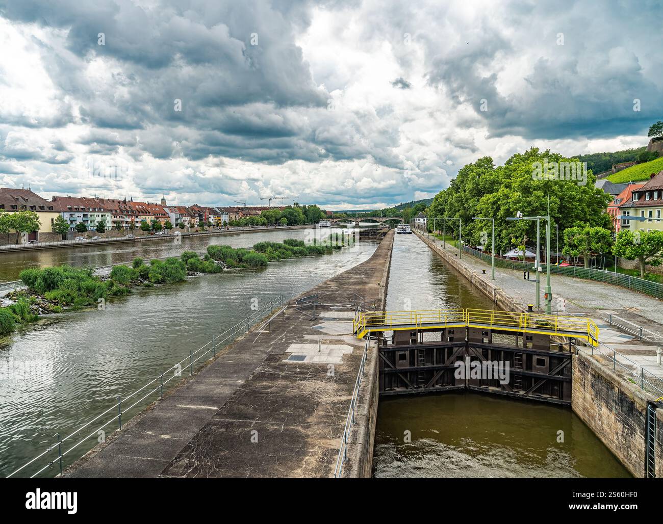 Un vivace lungomare urbano caratterizzato da un sistema di serrature, circondato dal verde e da edifici affascinanti, con spettacolari cieli nuvolosi in alto. Foto Stock
