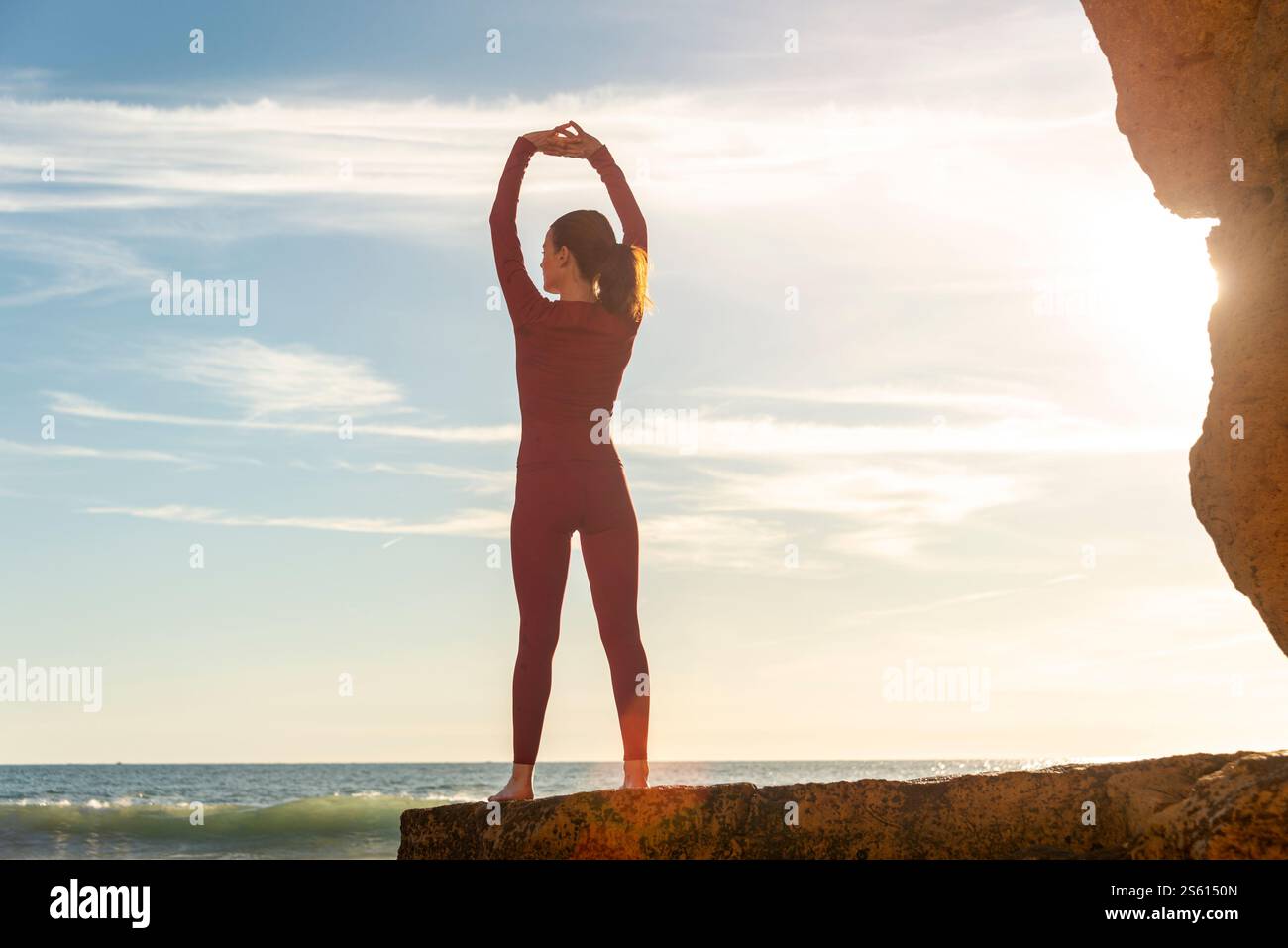 donna sportiva in piedi sulle rocce in spiaggia che si estende con le braccia sollevate, concetto di fitness all'aperto Foto Stock