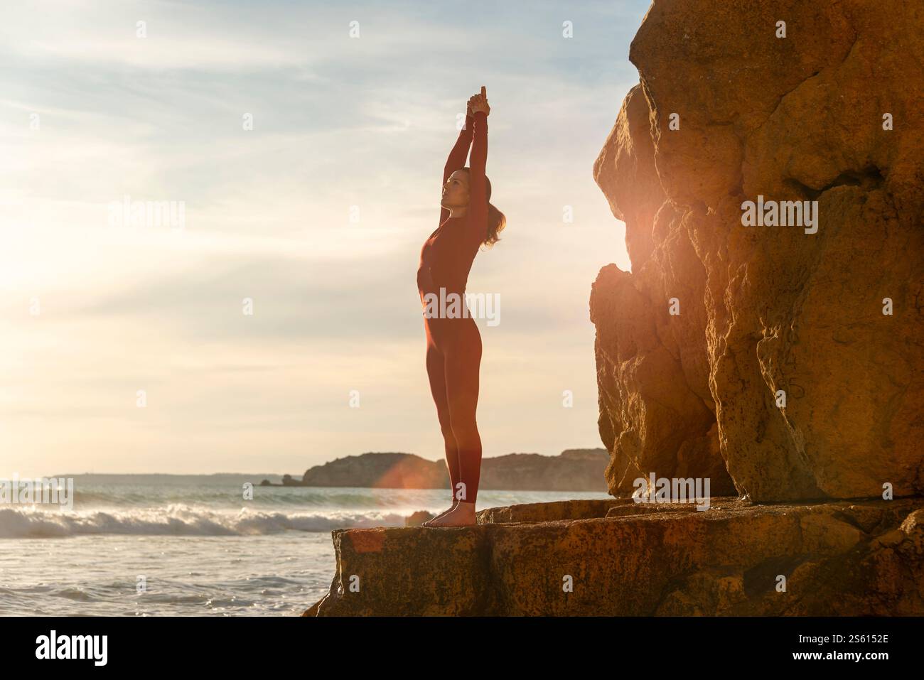donna in piedi su rocce sulla costa che fa una posa di montagna yoga braccia sollevate Foto Stock