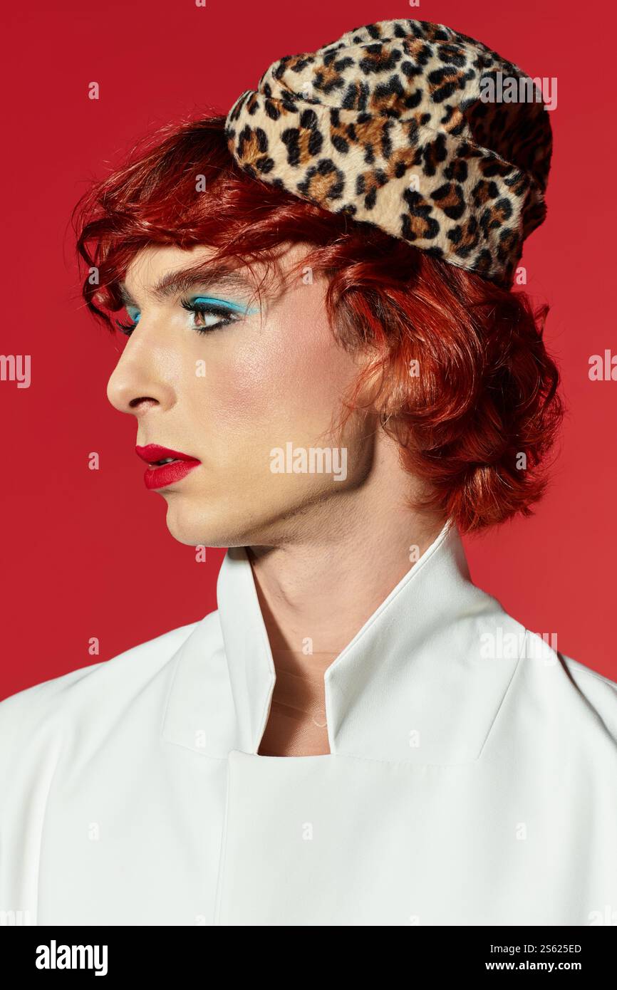 Giovane uomo vibrante con caratteristiche sorprendenti modella un esclusivo cappello con stampa leopardata e audaci scelte di trucco. Foto Stock