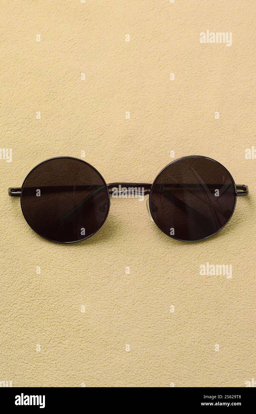 Gli eleganti occhiali da sole neri con occhiali rotondi si appoggiano su una coperta realizzata in morbido e soffice tessuto in pile arancione chiaro. Elegante immagine di sfondo in Foto Stock