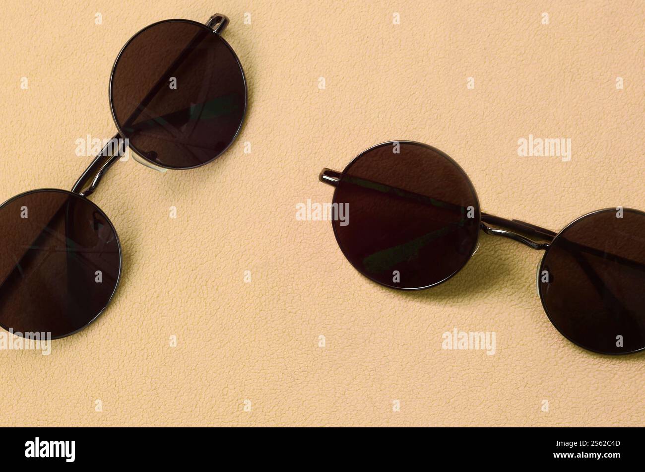 Due eleganti occhiali da sole neri con occhiali rotondi si trovano su una coperta realizzata in morbido e soffice tessuto in pile arancione chiaro. Immagine di sfondo alla moda Foto Stock