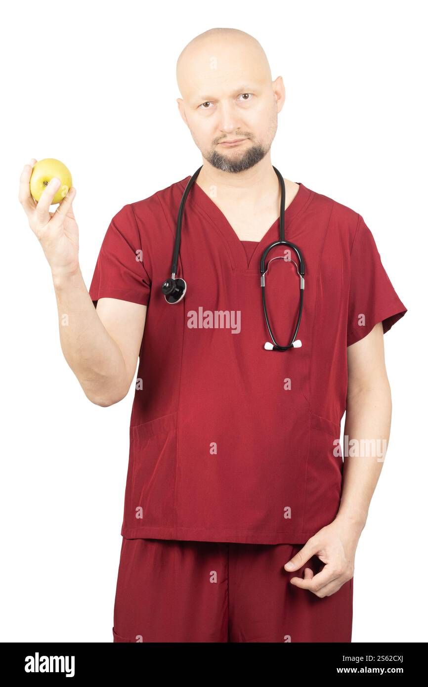 Un medico maschio calvo che indossa scrub medici rossi e uno stetoscopio intorno al collo sta tenendo una mela verde. Foto Stock