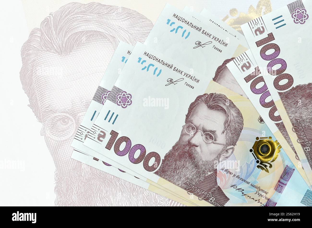 1000 banconote ucraine in hryvnias si trovano in una pila sullo sfondo di una grande banconota semi-trasparente. Presentazione astratta della moneta nazionale. Affari Foto Stock
