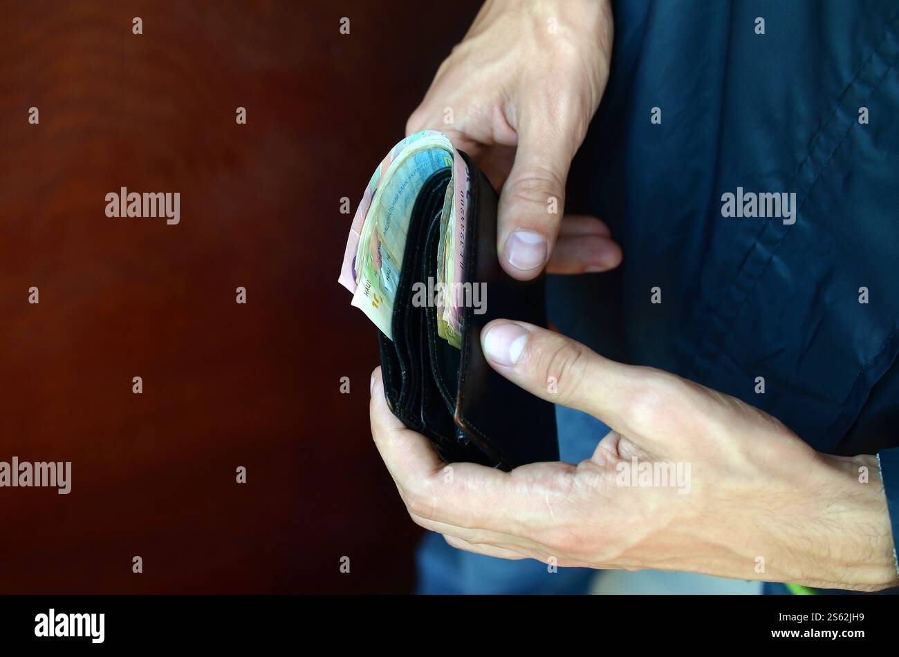 L'uomo tiene in mano un portafoglio in pelle nera con soldi ucraini o un ladro che ha rubato un portafoglio pieno di soldi. Crisi economica Ucraina e concetto di criminalità. Foto Stock