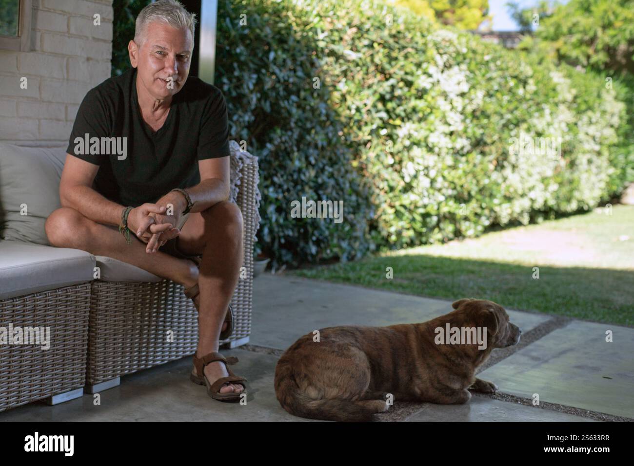 Uomo maturo che si gode l'estate a casa con il suo cane seduto nelle vicinanze e tenendolo in compagnia. Foto Stock