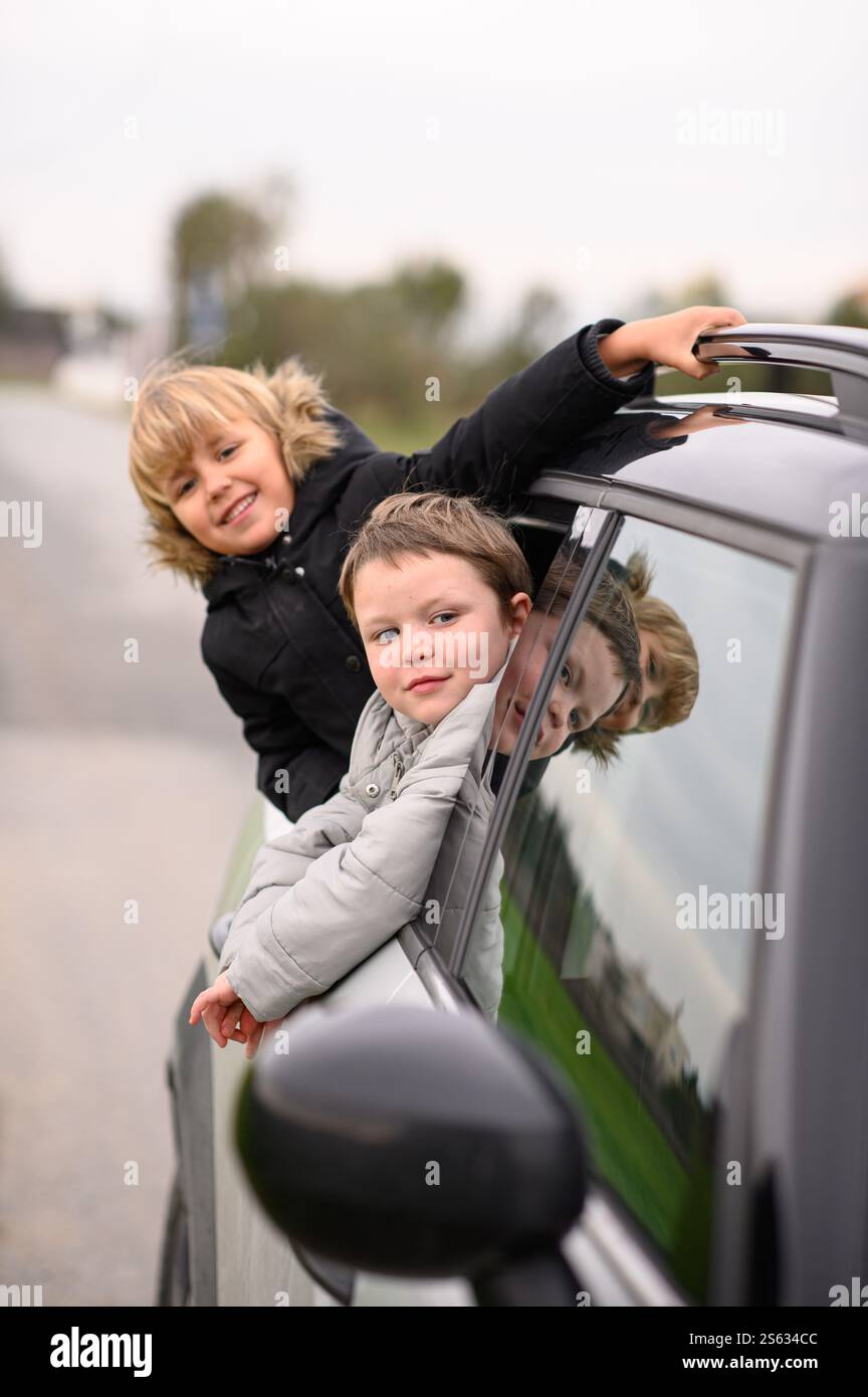I ragazzi si appoggiano ai finestrini di un'auto in movimento, ridendo e godendosi il vento freddo in un piccolo viaggio in auto Foto Stock