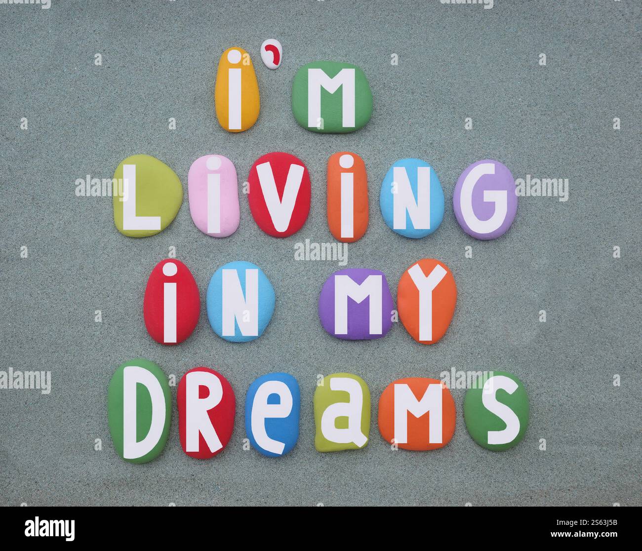 Vivo nel mio sogno, slogan creativo composto da lettere di pietra dipinte a mano multicolore su sabbia verde Foto Stock