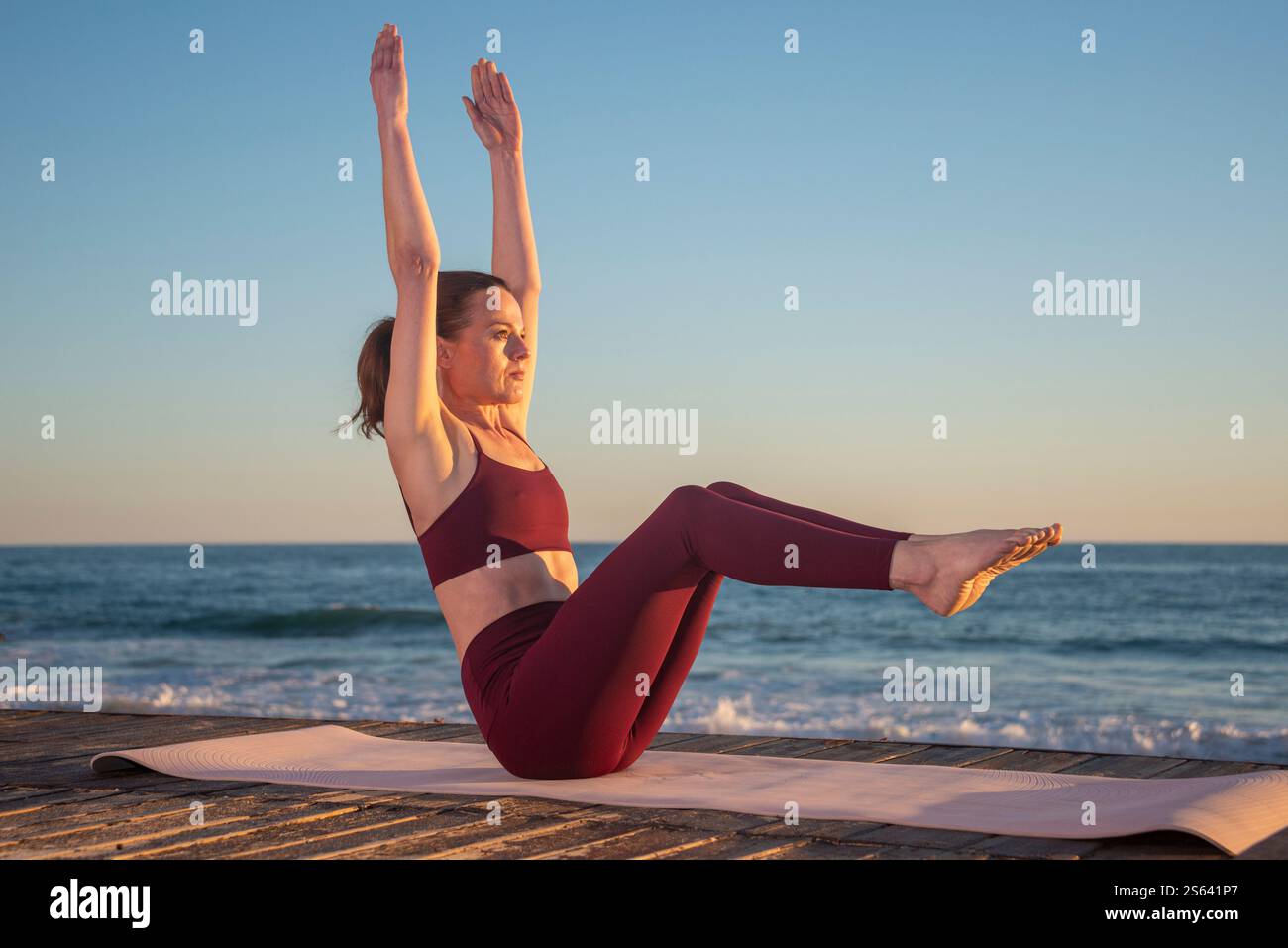 donna sportiva che fa posa in barca con le braccia sollevate all'aperto dall'oceano, allenamento muscolare Foto Stock