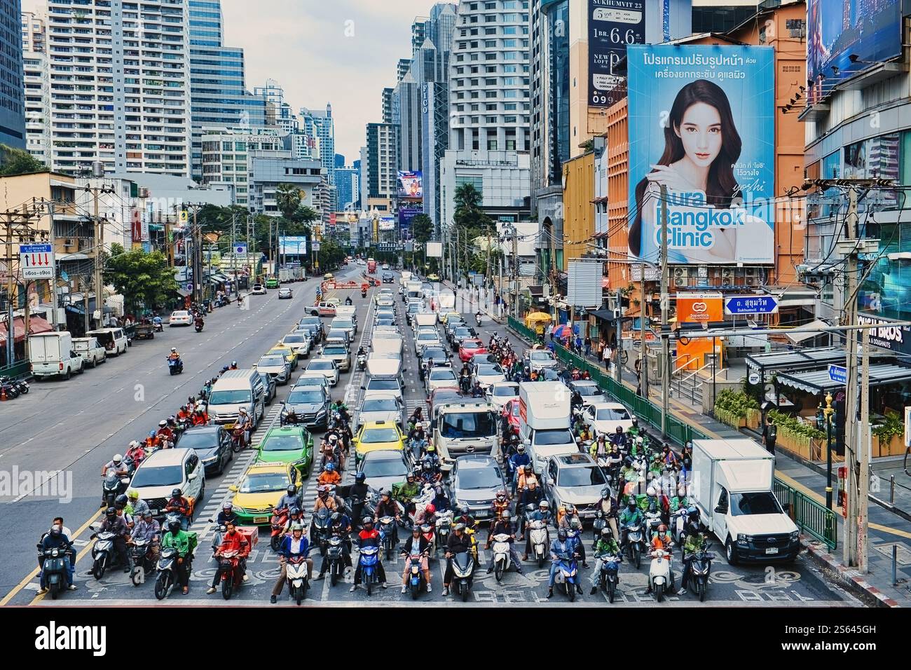 Una vista dall'intersezione di Asoke lungo Asok Montri Road, un'arteria principale a Bangkok, con grattacieli, grandi cartelloni e molte auto e motociclette Foto Stock